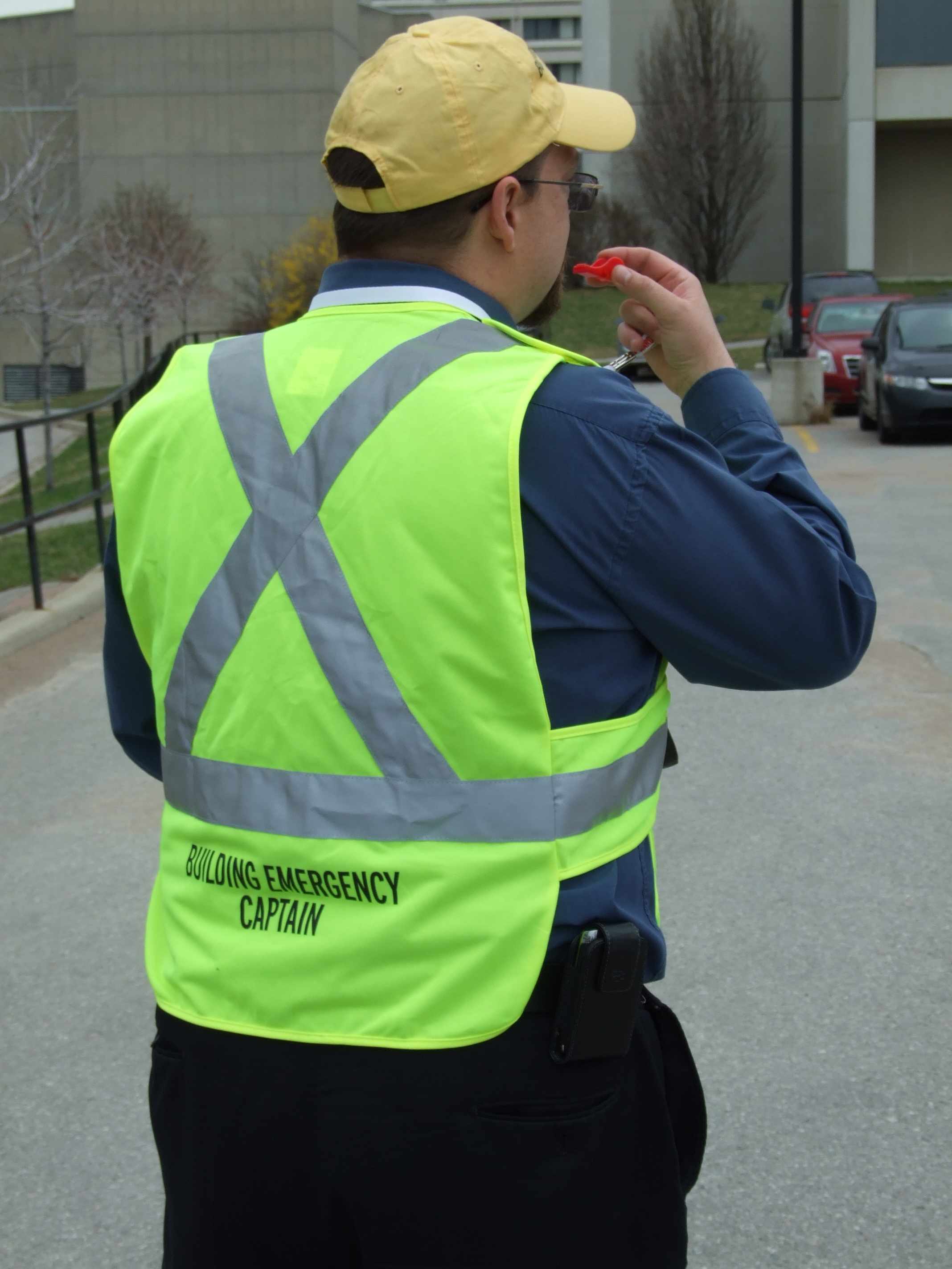 Person with a vest displaying building emergency captain blowing a whistle
